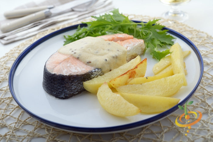 Salmon steak with mustard sauce, baked potato wedges, and mizuna mustard greens on a white plate