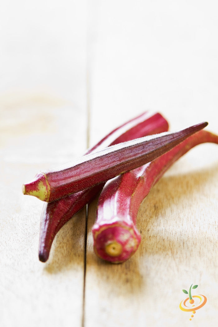 Close-up of Red Burgundy okra pods on wooden surface