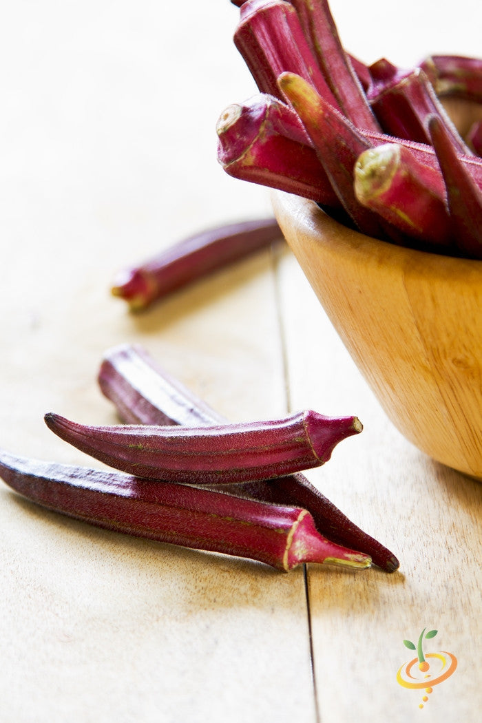 Fresh red burgundy okra pods in a wooden bowl on a light wooden surface